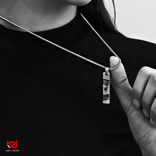 Person wearing a silver necklace with a pendant, against a black background