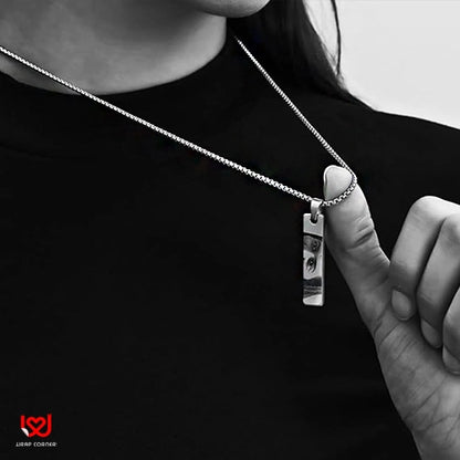 Person wearing a silver necklace with a pendant, against a black background