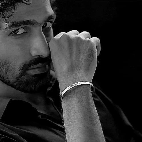 Man wearing a bracelet with an engraved message, looking thoughtful against a black background